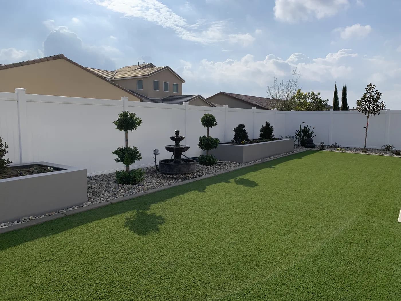 Tiered fountain and topiary in a river rock bed beside an artificial turf lawn