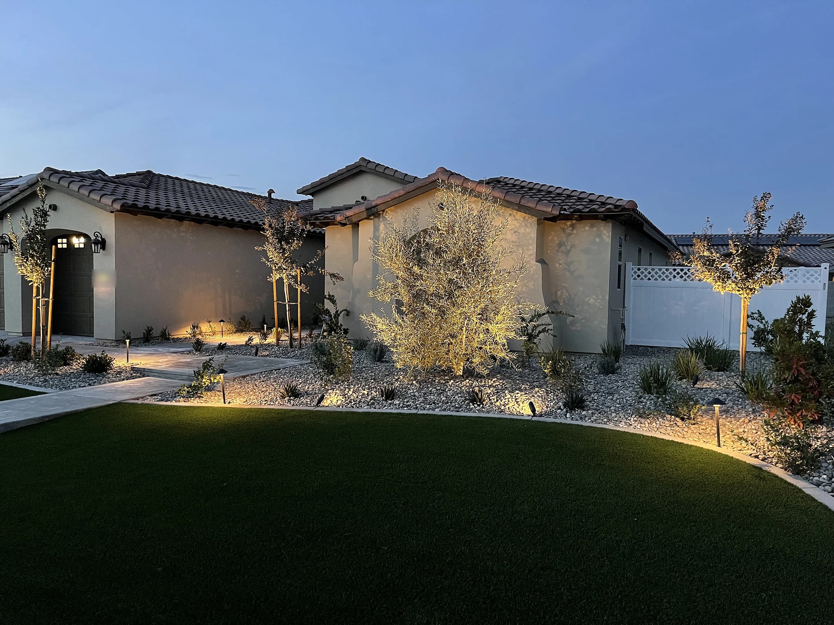 Front yard at dusk with uplit trees, path lights and artificial turf in front of a Bakersfield home