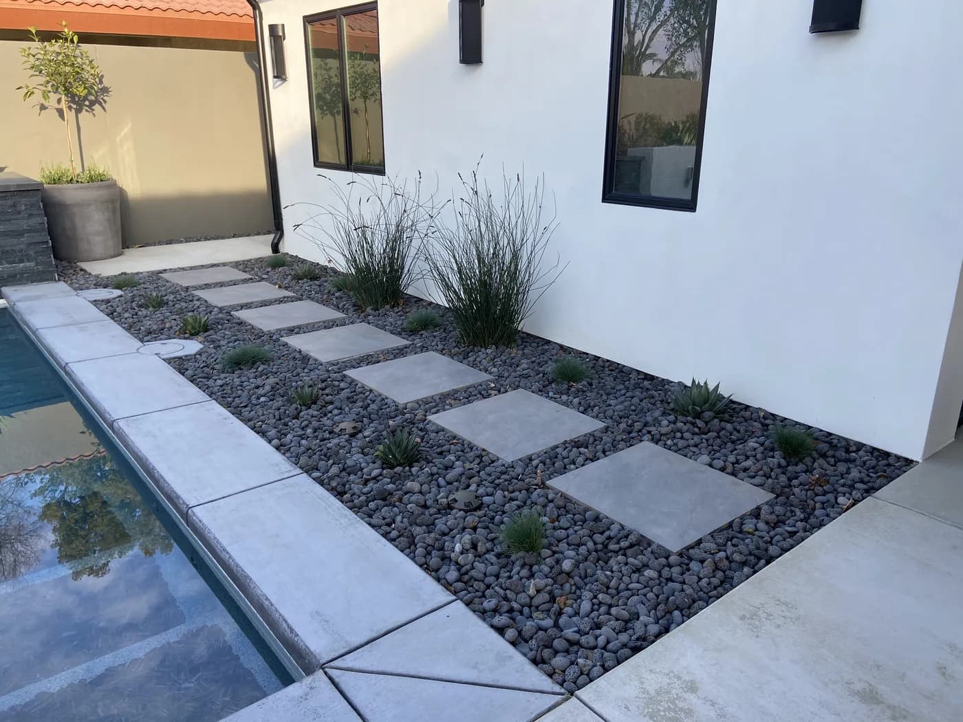 Square concrete pads set in gray gravel beside a pool, with grasses and agaves