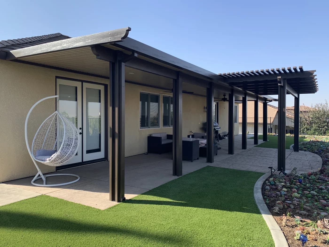 Bronze patio cover with a hanging egg chair beside a turf lawn and a succulent bed