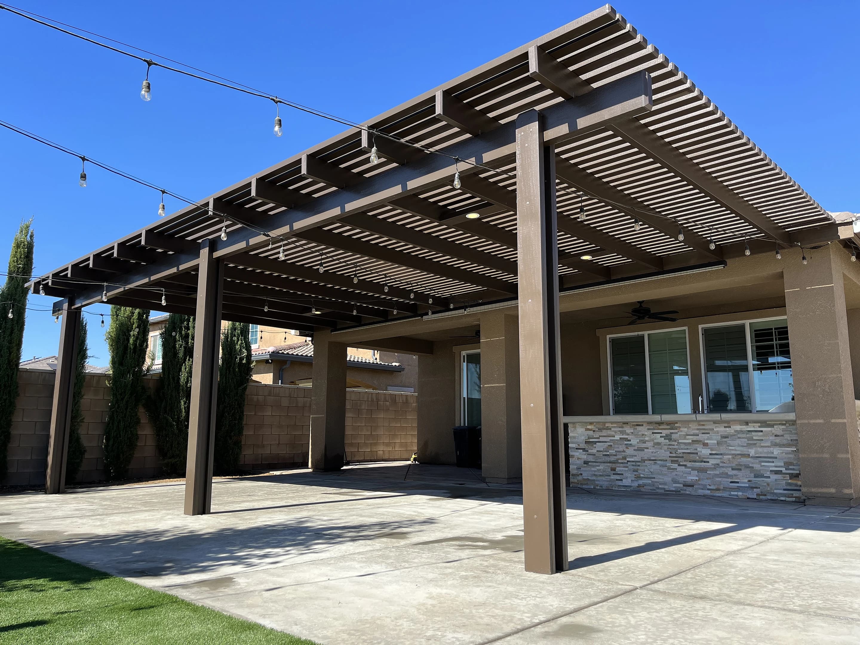 Lattice patio cover with string lights over a concrete patio and an outdoor kitchen